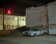 an old white car parked in front of a brick building with a neon sign on top