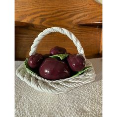 a white basket filled with plums on top of a bed