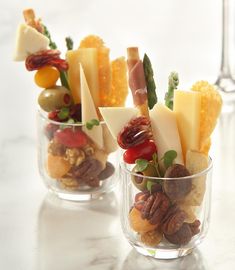 three small glass cups filled with different types of cheeses and nuts on top of a table