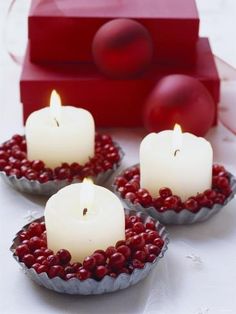 three white candles with red berries in bowls