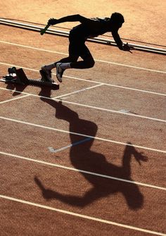 a man running across a tennis court with his shadow on the ground and in mid air