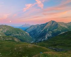 the mountains are covered in green grass as the sun sets