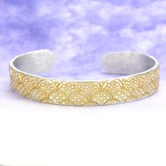 a gold and silver bracelet with filigrees on the outside, in front of a blue background