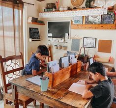 two young boys sitting at a wooden table with notebooks and pens in front of them