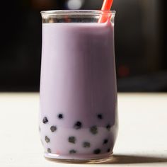 a purple drink in a glass with black dots on it and an orange straw sticking out of the top