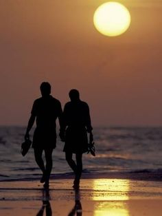 two people walking on the beach at sunset