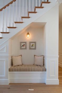 there is a bench under the stairs in this house with two pictures on the wall