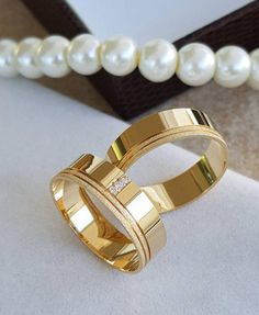 two gold wedding rings sitting on top of a table next to pearls and a necklace