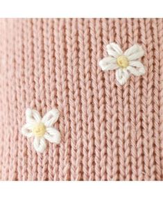 two white flowers are attached to the side of a pink knitted sweater with yellow and white buttons