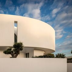 a white building with a tree in the foreground and clouds in the sky above it