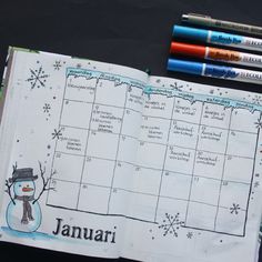 an open planner with snowman on it and three markers next to it, along with two pens