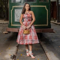 a woman standing in front of a green train car wearing a red and white dress