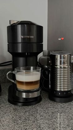 a coffee maker sitting on top of a counter next to a cup filled with liquid