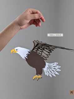 a hand holding an eagle cutout with a tag on it's string and another hanging from the ceiling