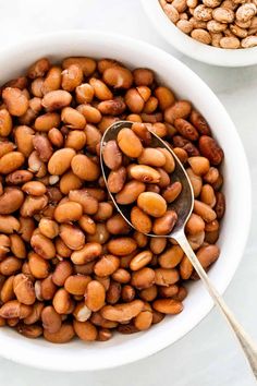 a white bowl filled with beans next to another bowl full of beans and a spoon