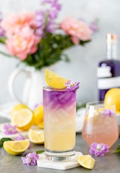 a drink with lemons and purple flowers in the background