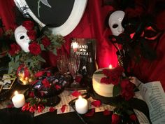 a table topped with cakes and candles on top of a table covered in red roses