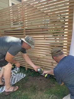 two men are working on a wooden fence