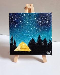 an easel with a painting on it that has a tent in the woods and stars above