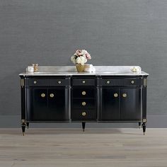 a black buffet table with marble top and gold accents on the legs, in front of a gray wall