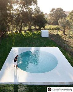 a woman standing in the middle of a pool surrounded by green grass and trees,