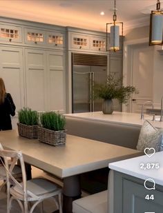 a woman standing in a kitchen next to a table with chairs and plants on it