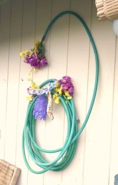 a green hose hanging on the side of a building with flowers attached to it's sides