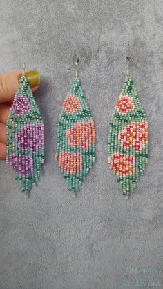 three beaded earrings are being held by a person's hand on a gray surface