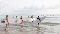 several surfers are walking into the ocean with their surfboards in one hand and holding boards in the other