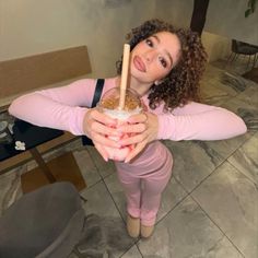 a woman in pink is holding a drink and posing for the camera with her arms crossed