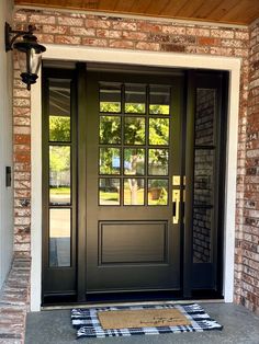 a black front door with two sidelights and a checkered rug on the ground