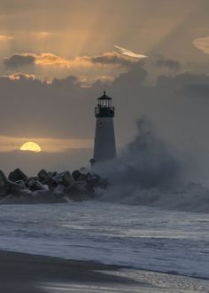 a light house on the beach with waves crashing in front of it and sun setting