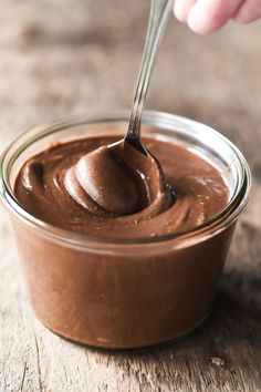 a spoon full of chocolate spread on top of a wooden table with a hand holding a spoon