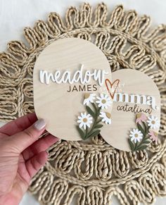 someone is holding up two wooden heart magnets with names and flowers on them in front of a woven doily