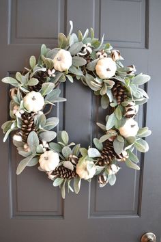 a wreath with white flowers and pine cones hanging on the front door's side