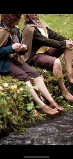 two people sitting on the edge of a stream with their feet up in the air