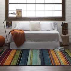 a bed sitting under a window on top of a wooden floor next to a rug