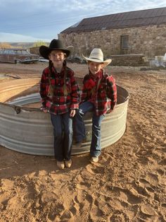 two young boys sitting in a barrel on the ground wearing cowboy hats and plaid shirts