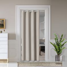 a room with a potted plant on the floor next to a white dresser and door