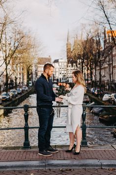 a man and woman standing next to each other on a bridge with flowers in their hands