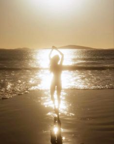 a woman standing on top of a sandy beach next to the ocean under a sun