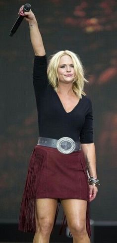 a woman in black shirt and red skirt on stage with her hand up to the sky