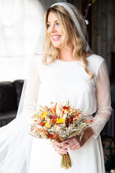 a woman in a white dress holding a bouquet of flowers and smiling at the camera