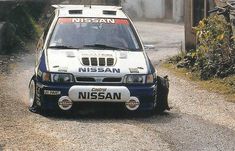 an old nissan car driving down a dirt road