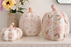 three painted pumpkins sitting on a shelf next to a vase with flowers in it