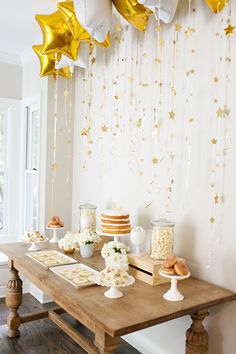 a wooden table topped with lots of cake and dessert covered in gold foil stars hanging from the ceiling