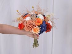 a woman's hand holding a bridal bouquet with orange, white and blue flowers