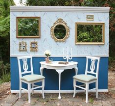 a table and two chairs sitting in front of a blue wall with mirrors on it