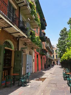 several tables and chairs on the sidewalk in front of buildings with green shuttered doors