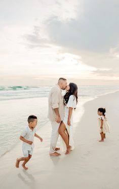 a man and woman kissing on the beach while two children run towards them with their feet in the sand